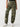 A person is shown from the shoulders down wearing Sanctuary Clothing's Cyber Cargo Renew Camo pants, which feature large front and side pockets. They are also sporting a black top and white sneakers with green detailing. The background is plain and light-colored.