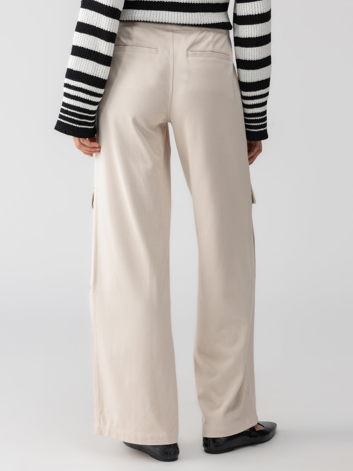 Rear view of a person wearing a black and white striped long-sleeve sweater and Sanctuary Clothing's Ponte Travel Cargo Toasted Almond wide-leg pants with side pockets. The person is also wearing black shoes, standing against a plain light background.