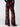 A person wearing the Sheer Nights Pant Moody Rose by Sanctuary Clothing, featuring flowy, sheer black fabric adorned with bold red floral patterns. They are also dressed in a black long-sleeved top and black shoes, set against a plain white background.