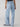 A person wearing the Tailored Renewal Jean Mirage from Sanctuary Clothing stands with their back facing the camera. The light blue wide-leg jeans have two back pockets and are paired with a black top. The person is standing against a plain, light-colored background.