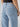 Close-up of a person wearing the Tailored Renewal Jean Mirage by Sanctuary Clothing, shown from the back. The light blue denim jeans feature two back pockets and light stitching. The person is also clad in a dark top, with their right hand partially visible.