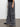 A person is wearing the "speed denim cargo odyssey" by Sanctuary Clothing, featuring oversized, gray, wide-leg cargo jeans with multiple large pockets. They are also styled with a black top and black shoes, set against a plain light-colored wall and a concrete floor.