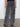 A person is wearing the speed denim cargo odyssey jeans by Sanctuary Clothing in a gray stonewashed finish with multiple side pockets, along with black shoes, standing on a gray floor. The individual's back faces the camera.