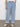 A person in Sanctuary Clothing's "Luna Cuffed Jeans Blue Moonlight," featuring wide-leg and cuffed hems, pairs them with a tucked-in white shirt. They stand against a white backdrop with one hand in their pocket, wearing beige woven flats to complete the look.