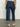 A person is seen from the back wearing Sanctuary Clothing's Luna cuffed denim pant solstice, featuring high-waisted, wide-legged dark denim with large back pockets and rolled cuffs. They pair it with light woven shoes on a smooth gray floor against a plain background.