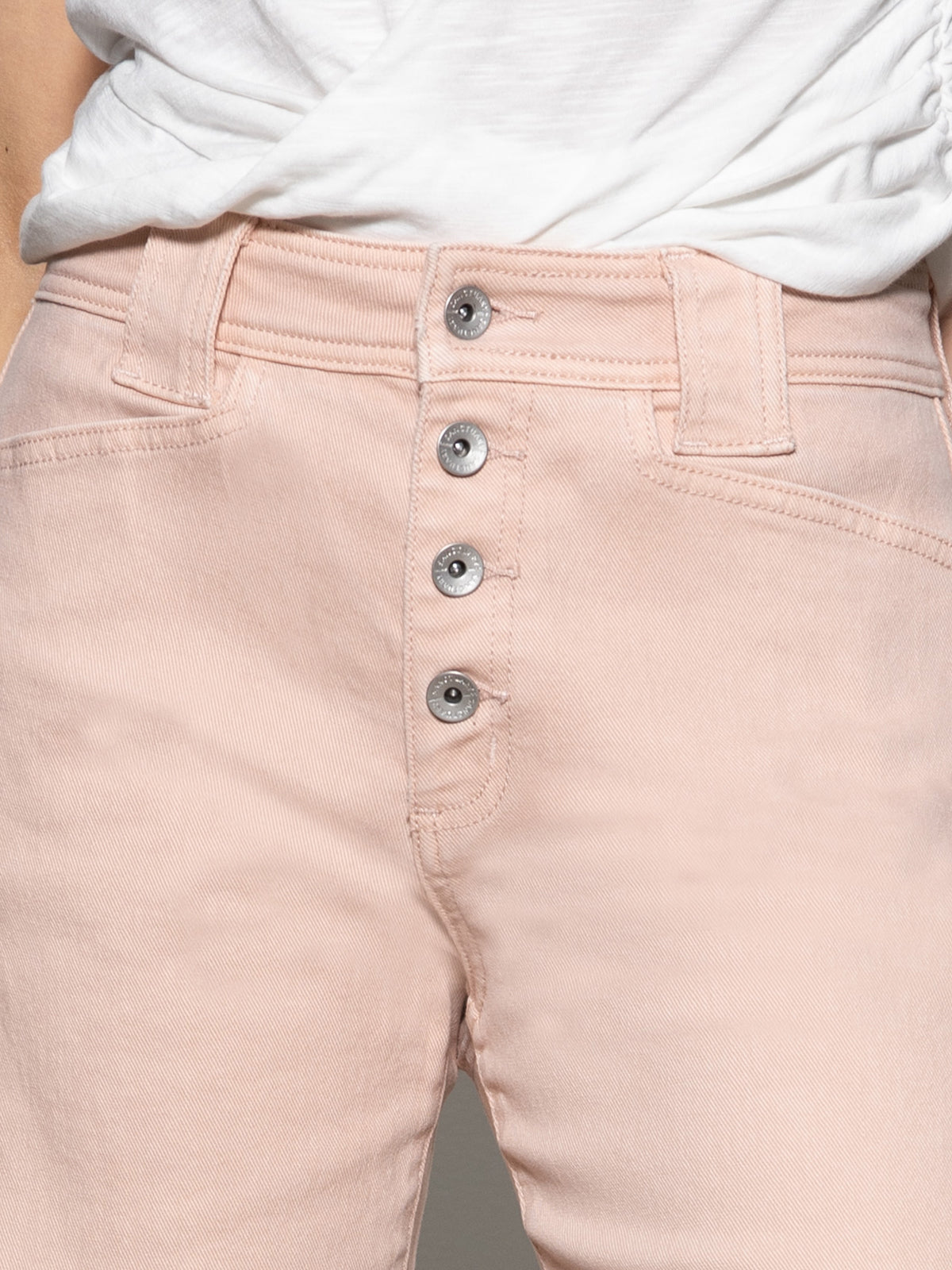 Close-up of someone wearing Sanctuary Clothing's luna cuffed jeans in earth pink, featuring a high waist and four visible metallic buttons, paired with a white tucked-in shirt.