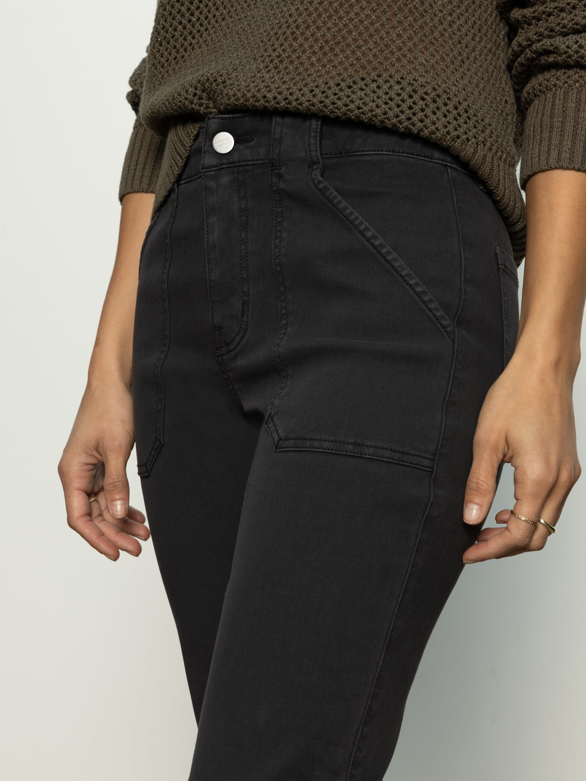 A person is wearing the Sanctuary Clothing sculpted Hayden straight crop pant in black with front pockets and a textured brown sweater. They have a ring on one finger and are posing against a neutral background.