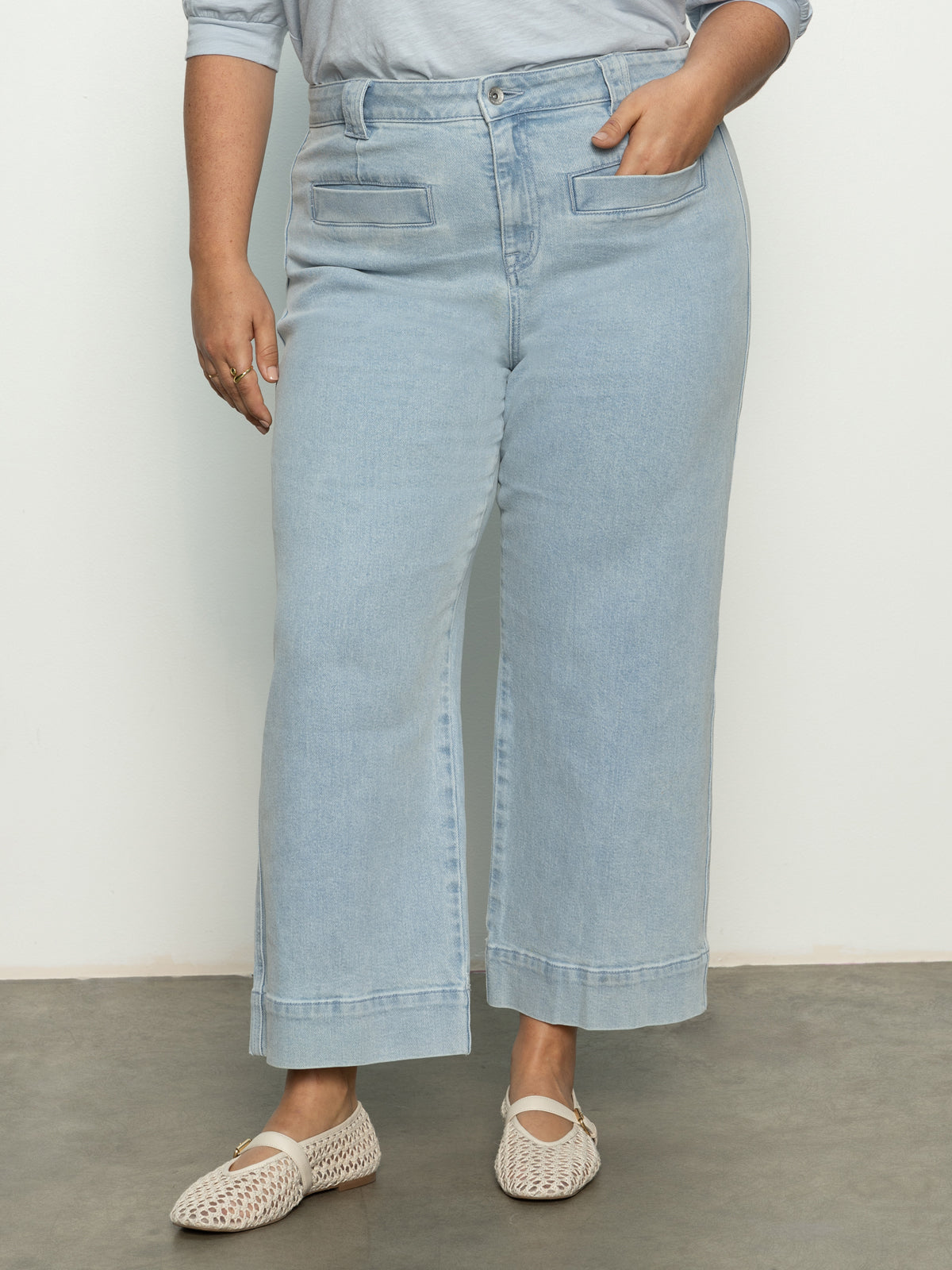 A person wearing Sanctuary Clothing's Voyage Crop Pant in Winners Circle from the Inclusive Collection stands with one hand in a pocket. They pair it with a matching shirt and open-weave cream-colored flat shoes against a plain background.