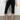 A person wearing Sanctuary Clothing's clipper ponte capri pant in black and a white and black knitted top, paired with black woven shoes, stands against a plain gray background with one hand on their hip and the other arm by their side.