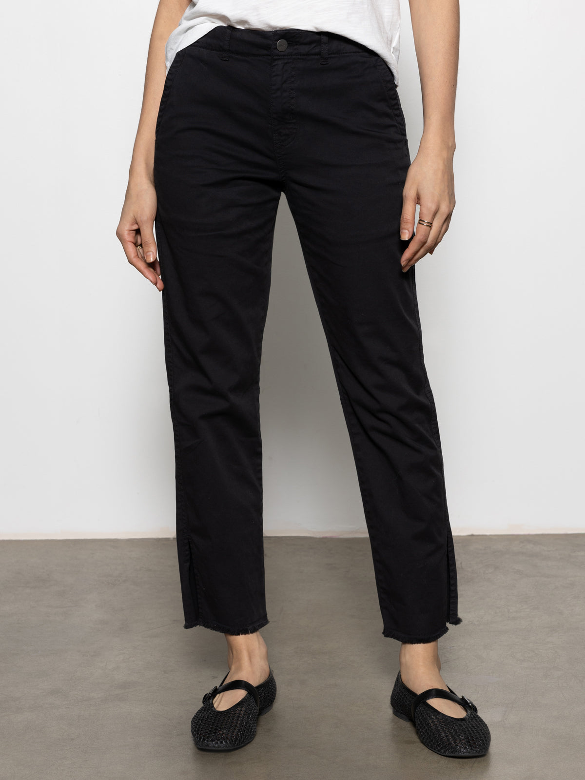 A person stands against a neutral background wearing Sanctuary Clothing's Trade Maker Pant in black, featuring a relaxed fit. They pair it with black shoes and a white top, with their hands resting by their sides.