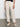 A person stands against a neutral background wearing Sanctuary Clothing's trade maker pant in light oat. Their upper torso isn't visible; one hand rests by their side while the other touches their pocket. They pair the pants with white woven flats.