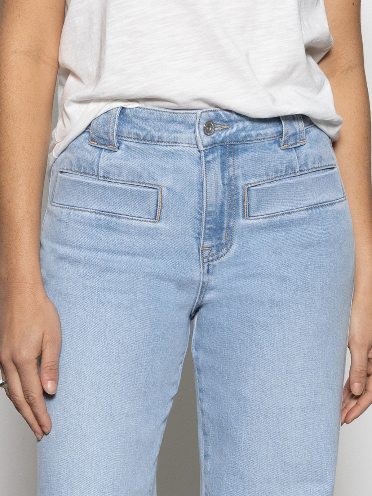 A person wearing Sanctuary Clothing's "Voyage Full Length Pant" in the color Wishful Thinking is paired with a white top. The light blue jeans feature wide belt loops and two horizontal front pockets, and the person stands with their arms relaxed at their sides.