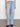 A person in Sanctuary Clothing's "voyage full length pant wishful thinking" light blue jeans with front flap pockets and a white shirt stands against a plain white wall. They are wearing black shoes, with the focus on the jeans from the waist down.