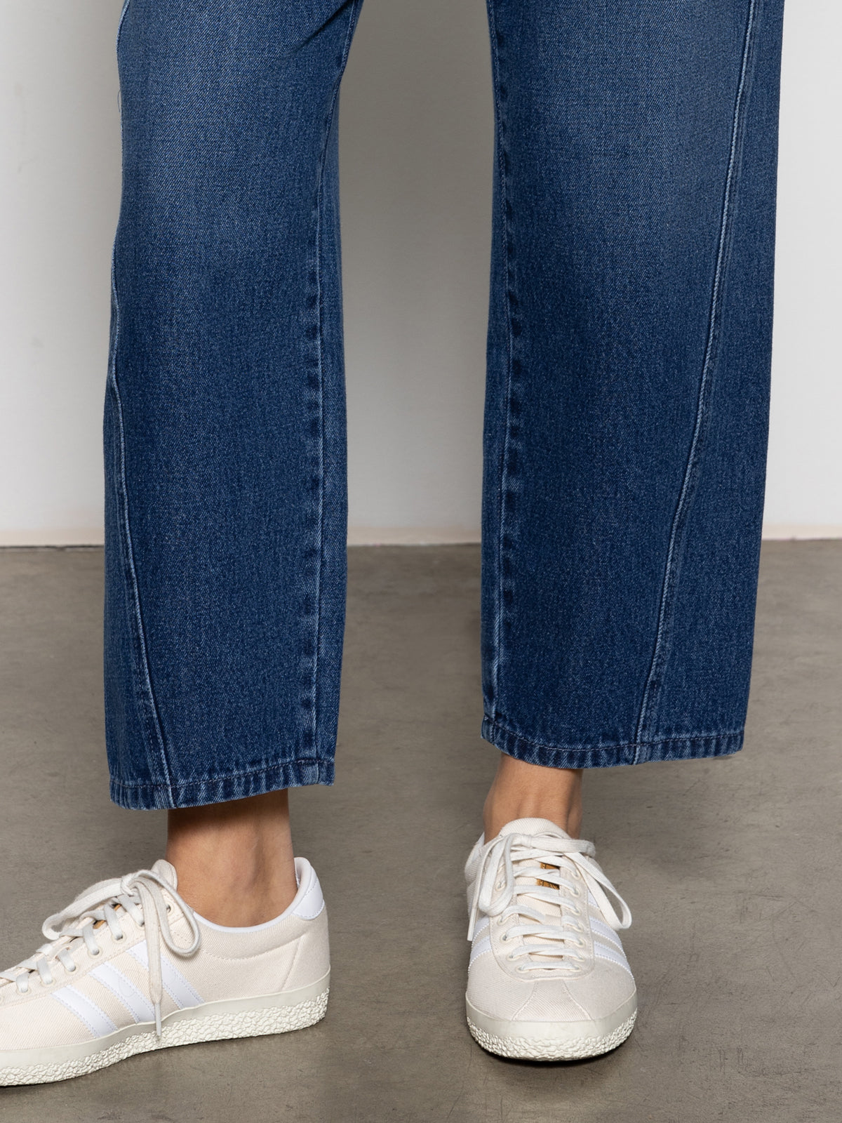 An individual in Sanctuary Clothing's district column ankle jeans and white sneakers stands on a concrete floor.