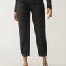 A person is wearing the "Sahara Tapered Pant Black" by Sanctuary Clothing, which features a relaxed fit and cropped length, complete with convenient pockets. They have paired it with a black long-sleeve top and stylish black pointed-toe shoes with ankle straps. The backdrop is a plain white setting.