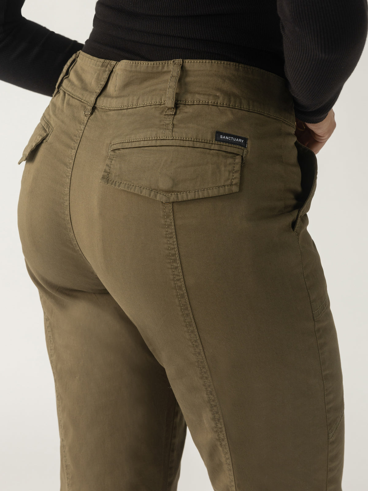 A person wearing the Sahara Tapered Pant in Burnt Olive by Sanctuary Clothing, along with a black top, is shown from the waist down against a plain background.