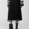 A person is wearing a Sanctuary Clothing Tulle Pleated Midi Skirt in Black, black mid-calf heeled boots, and a long-sleeved black and white striped sweater. The photo is taken from the shoulders down against a plain background.