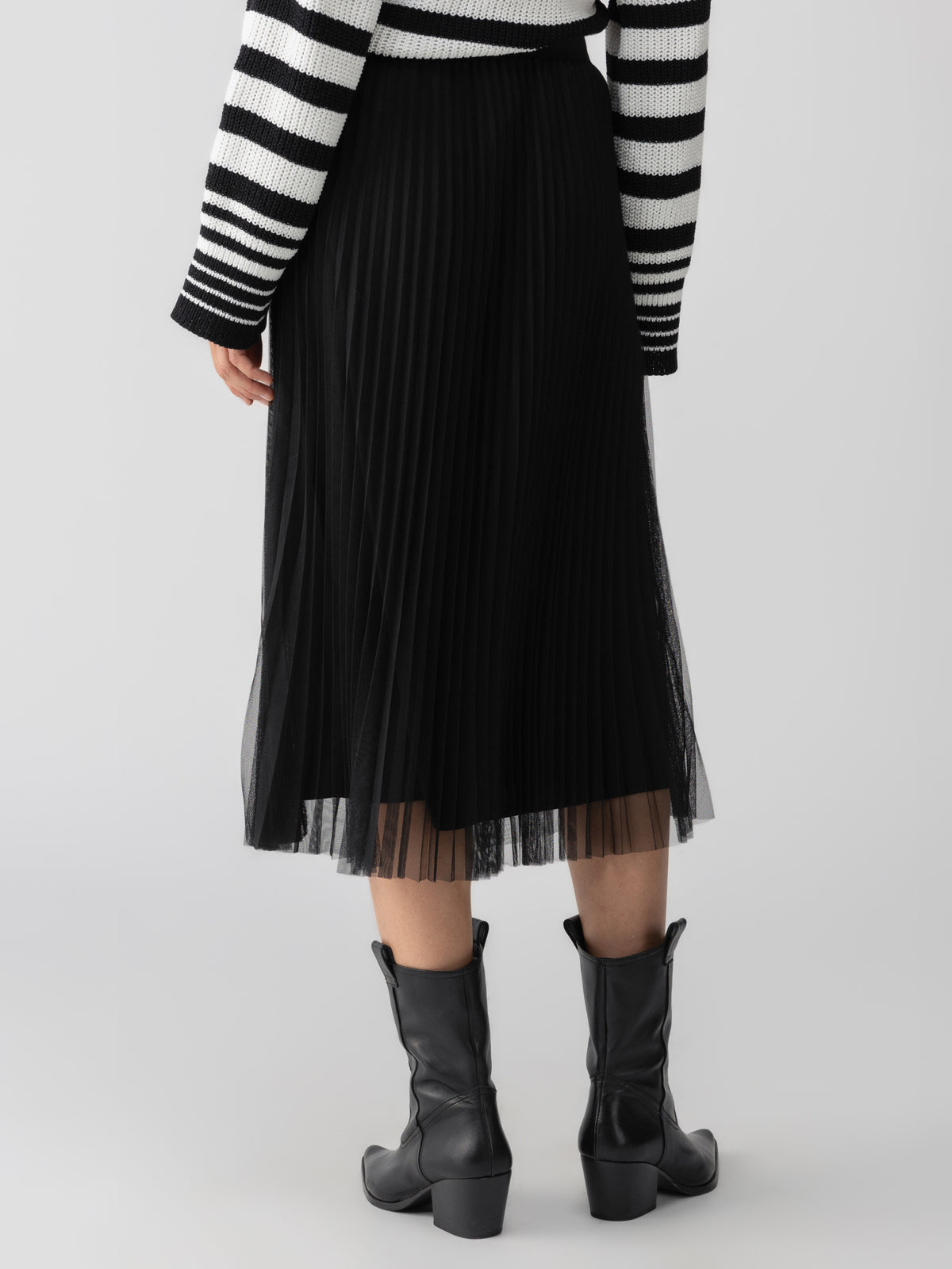 A person wearing the Tulle Pleated Midi Skirt Black by Sanctuary Clothing stands with their back to the camera. They also wear a black and white striped sweater and black ankle boots, all set against a plain background.