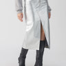 A person is wearing Sanctuary Clothing's "Leather Like Midi Skirt Silver," featuring a front slit, paired with a gray textured sweater and black knee-high boots. The outfit is styled against a plain white background.