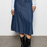 A person wearing the flora denim skirt happy hour by Sanctuary Clothing, featuring visible seam details, pairs it with a light blue and white striped long-sleeve top and black ankle boots, standing against a plain background.