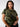 A person with long hair is wearing "The Perfect Tee Hiker Camo Inclusive Collection" by Sanctuary Clothing and black pants. They have gold hoop earrings and are standing against a plain light grey background. Their expression is neutral, and they are looking directly at the camera with one hand resting on their stomach.