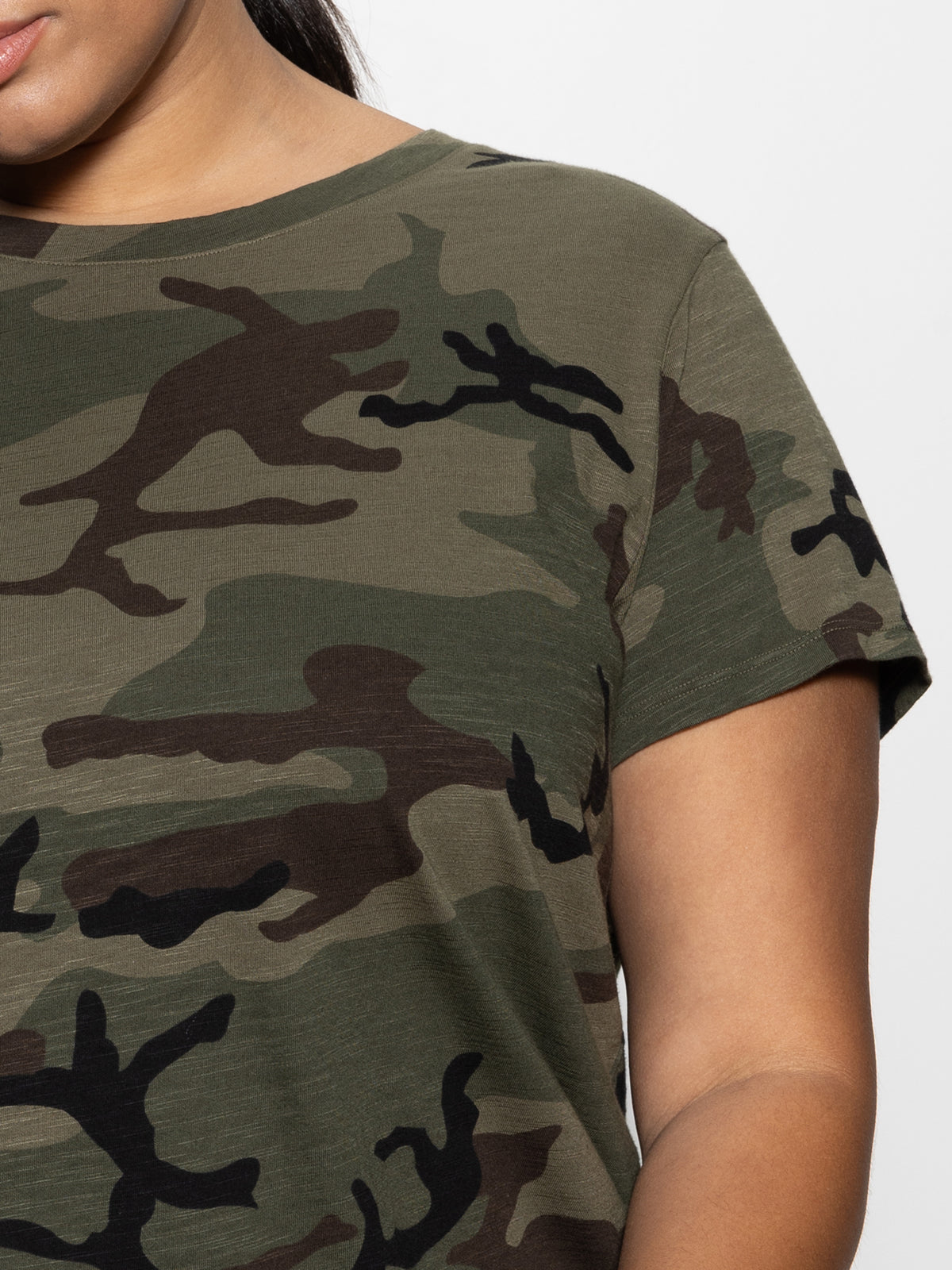 A person models the Perfect Tee from Sanctuary Clothing's Hiker Camo Inclusive Collection. The shirt, with its abstract green and brown camouflage patterns, covers their upper torso and part of their left arm against a plain white background.