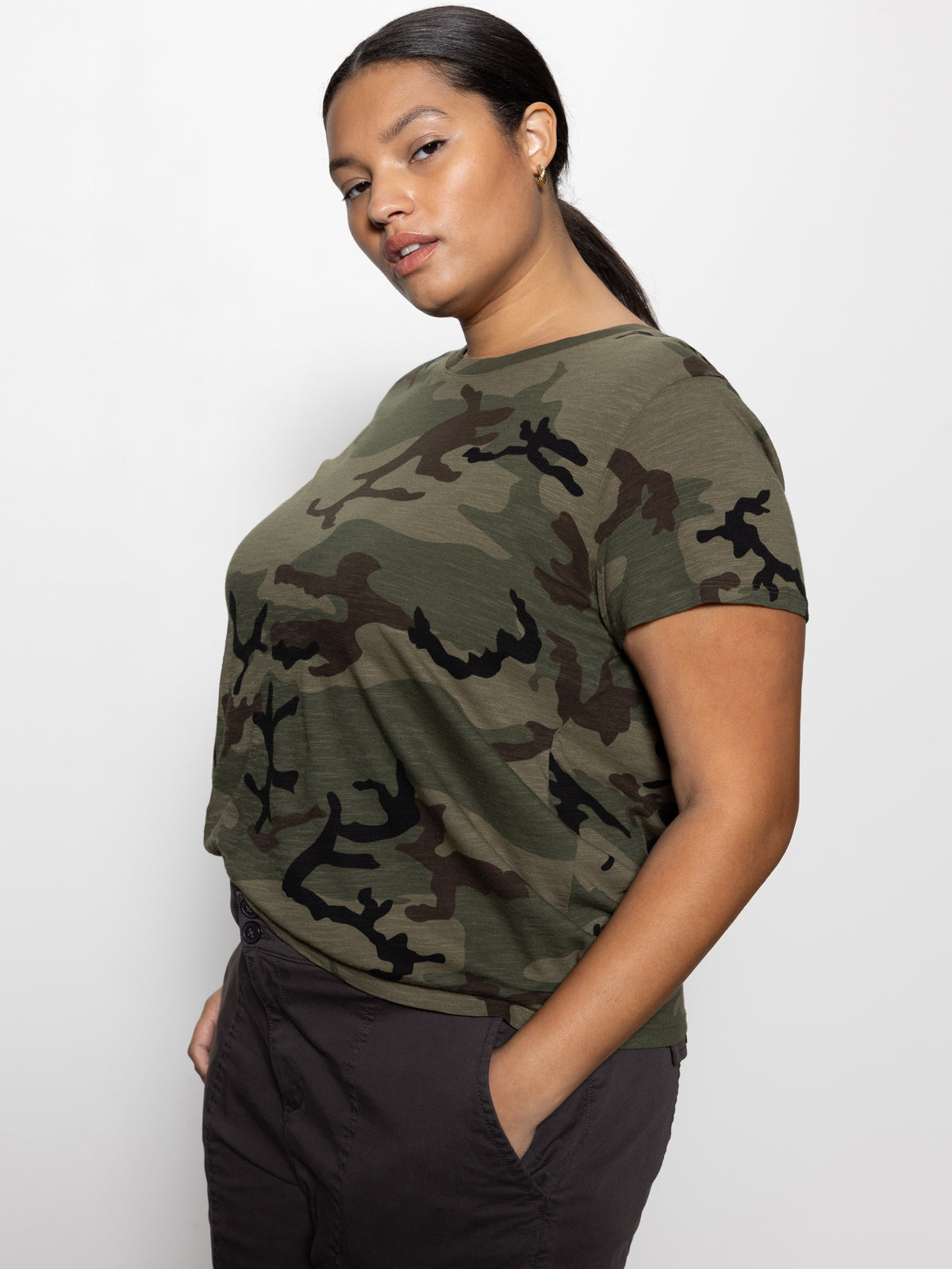 A person with dark hair poses against a plain background, wearing Sanctuary Clothing's Perfect Tee from the Hiker Camo Inclusive Collection and dark pants. They look confidently at the camera with a neutral expression.