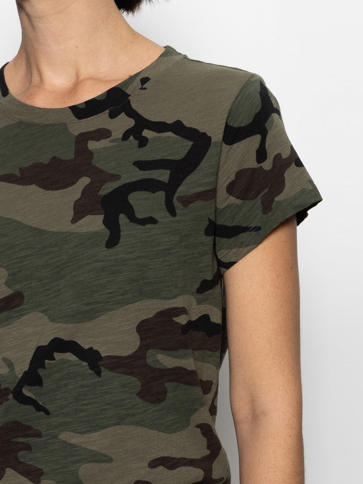 A person is wearing Sanctuary Clothing's "the perfect tee hiker camo" featuring a green and brown camouflage pattern. Only the shoulder, part of the chest, and arm are visible against a plain white background.