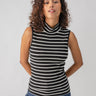 A person with curly hair is wearing the Essential Sleeveless Mock Neck Black Chalk Stripe top by Sanctuary Clothing, paired with blue jeans. They are standing against a plain gray background with their hands resting on their hips.