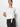 A person models in front of a plain white background, wearing the "All Day Tie Tee" in white from Sanctuary Clothing's Inclusive Collection. They've paired it with dark pants and have dark hair pulled back, looking slightly to the side.