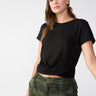 A person with shoulder-length brown hair is wearing a Highstreet Tee Black by Sanctuary Clothing and camouflage-patterned pants. They have a neutral expression and are standing against a plain, light-colored background.