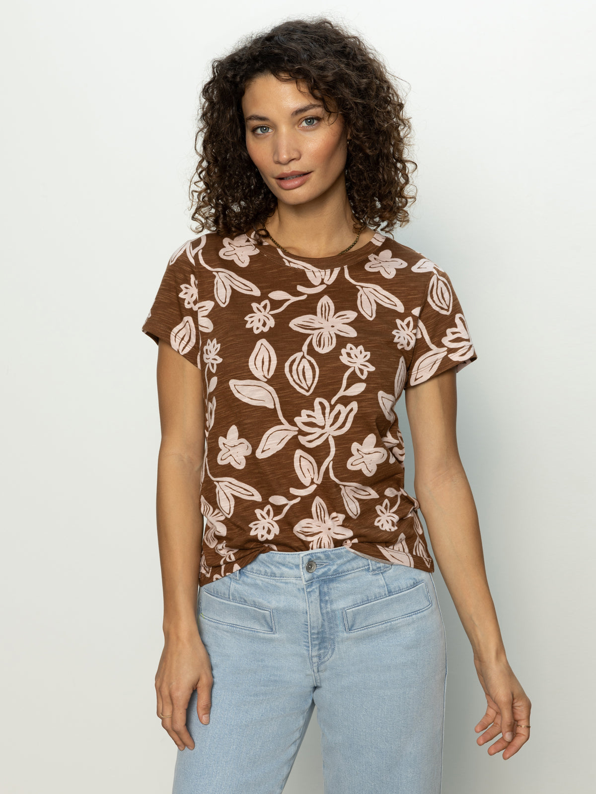 A person with curly hair is wearing Sanctuary Clothing's "the perfect tee earth ivy" and light blue jeans, standing against a plain white background.