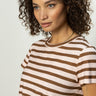 A woman with curly hair wears "The Perfect Tee" in earth pink sepia stripe from Sanctuary Clothing, gazing thoughtfully to the side against a plain background.