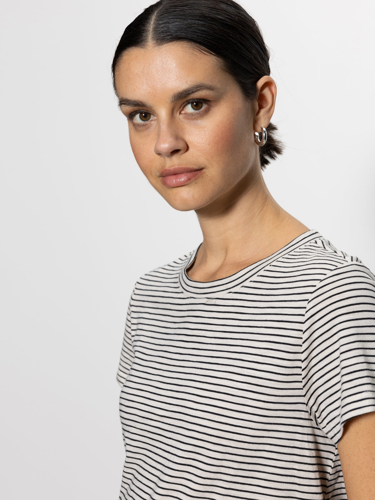 A person with dark hair tied back wears the perfect tee pumice stone black stripe by Sanctuary Clothing, looking directly at the camera against a plain light-colored background.