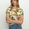 A person wearing Sanctuary Clothing's "The Perfect Tee Precious Camo" and blue jeans stands against a plain background with arms crossed, gazing forward.