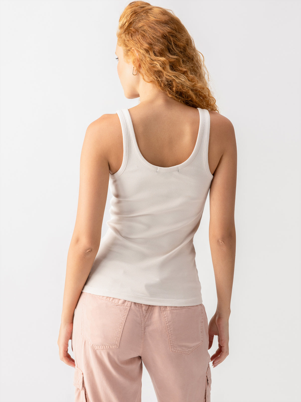 A person with curly, light-colored hair is wearing the My Kind Of Tank Crystal Stone by Sanctuary Clothing and pink pants. They are standing and facing away from the camera against a plain white background.