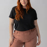 A woman with long red hair is standing against a plain background. She is wearing the Perfect Mesh Tee Black from the Inclusive Collection by Sanctuary Clothing and brown cargo pants. Her expression is neutral, and her hands are relaxed by her sides.