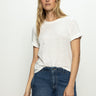 A person with long blonde hair is wearing a Sanctuary Clothing Perfect Tee Remix in white and blue jeans. They stand against a plain background, looking directly at the camera with a neutral expression.