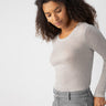 A woman with curly hair is wearing the Femme Crew Tee Heather Grey by Sanctuary Clothing and gray jeans. She is looking down and slightly to her right with a relaxed expression, against a plain, light-colored background.