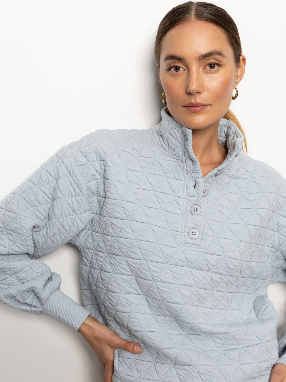 A person with brown hair tied back is wearing the Quilted Button Up Popover Top in Pearl Blue from Sanctuary Clothing. They are standing against a plain white background, looking directly at the camera with a neutral expression.