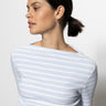 A person with dark hair tied back is wearing a long sleeve boatneck t-shirt in sky blue and white stripe by Sanctuary Clothing, along with small hoop earrings. They are looking to the side against a plain white background.