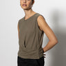 A person with dark hair tied back is wearing the Sanctuary Clothing draped tank in burnt olive with black pants. They pose against a white background, one hand on their hip, with a neutral expression.