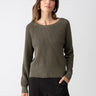 A person with long, brown hair is wearing the Everyday Openwork Sweater Kalamata by Sanctuary Clothing paired with black pants. With one hand in their pocket, they look confidently at the camera against a plain white background.