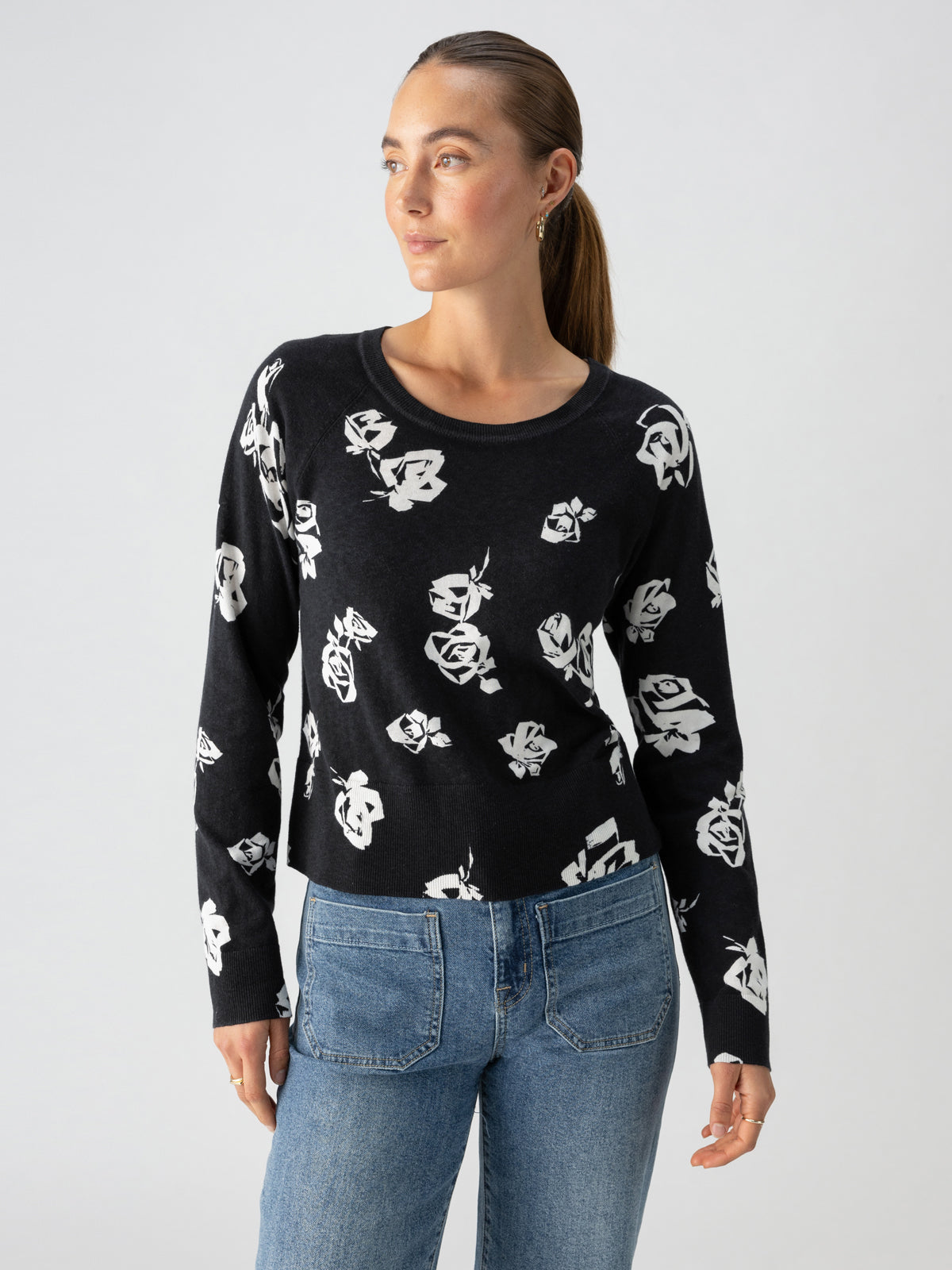 A person is wearing the All Day Long Sweater Rose Pop by Sanctuary Clothing and light blue jeans. They have their hair pulled back into a ponytail and are looking to the side against a plain background.