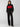 A person stands against a plain backdrop wearing the Sanctuary Clothing Stay Cozy Sweater Black Red Stripe. They are also wearing black wide-leg cargo pants and black shoes. Their hands are in their pockets, and their hair is down.