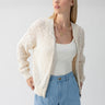 A person with light-colored hair wears the Stepping Out Bomber Eco Natural from Sanctuary Clothing over a white tank top and light blue pants. They are looking to the side with a neutral expression against a plain background. Multiple gold necklaces accessorize the outfit.