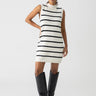 A person stands against a plain white background, wearing the Life Is Easy Swtr Dress Chalk Black Stripe by Sanctuary Clothing. They are also wearing tall, black boots and have their hand on their hip.