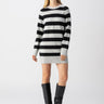 A person is posing in the Sanctuary Clothing So Soft Sweater Dress Heather Grey Black Stripe and black knee-high boots. They have long hair and are standing against a plain white background.