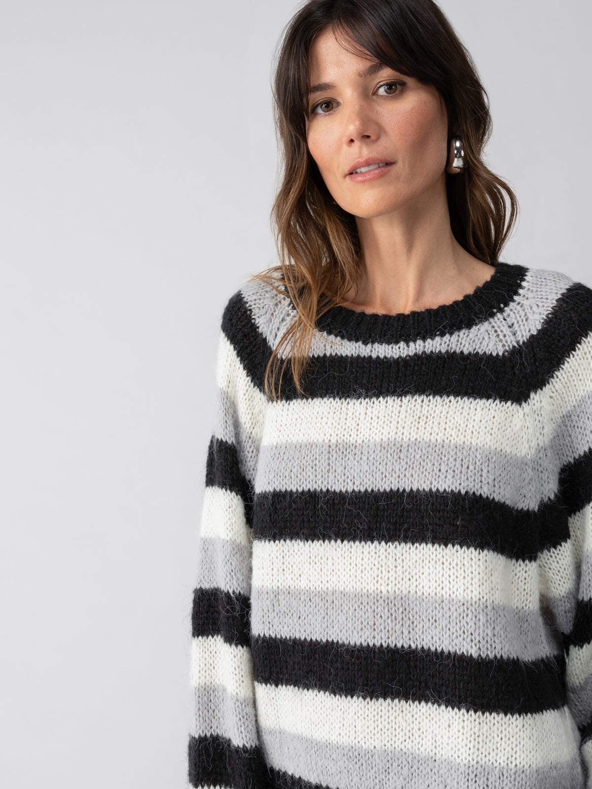 A person with long hair wearing the Picture This Stripe Sweater in Ash Multi Stripe by Sanctuary Clothing is looking toward the camera with a neutral expression. The background is plain white.