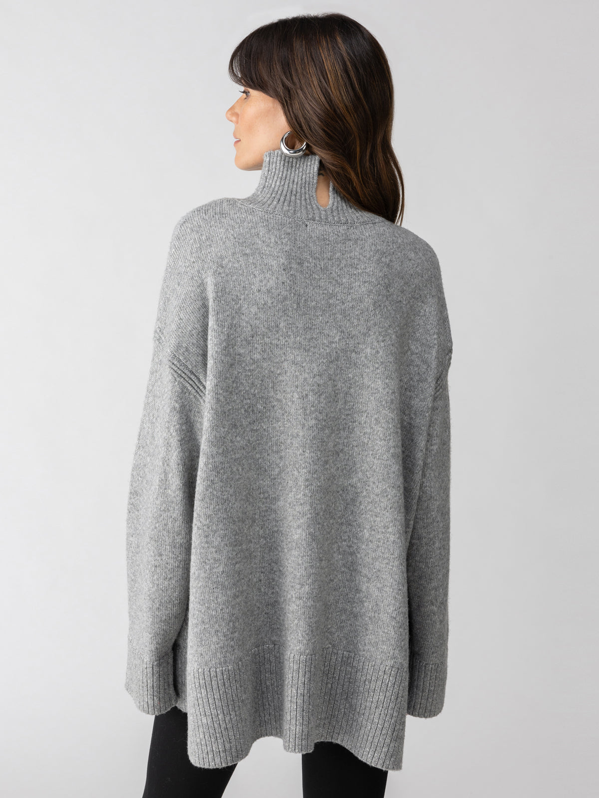 A person with long dark hair is wearing the Perfect Tunic Heather Ash by Sanctuary Clothing, featuring a loose fit and a high collar with ribbed edges. They are facing away from the camera against a plain light background.